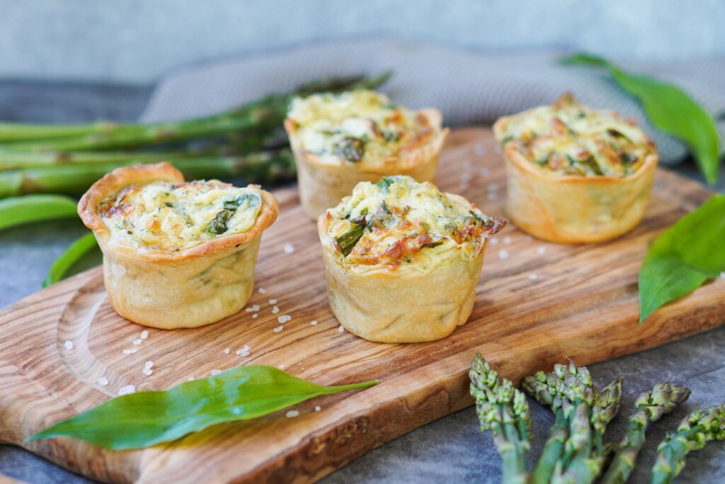 Auf dem Bild sind Quiches mit Bärlauch auf einem Holzbrett zusehen 
